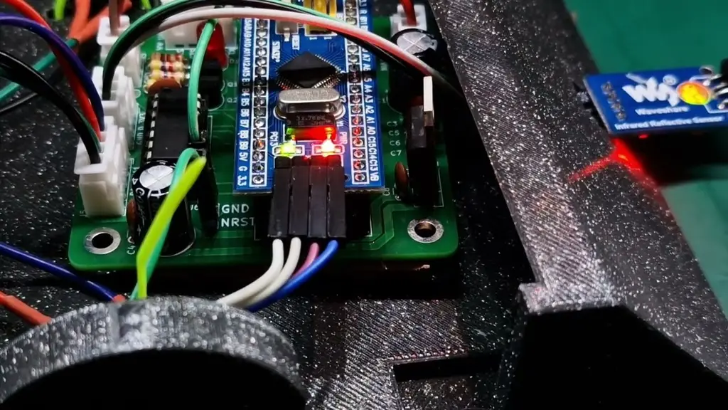 Close-up of the sumo robot's STM32 control board on the bench, wired with jumper leads to WisentWire and an infrared reflective sensor.